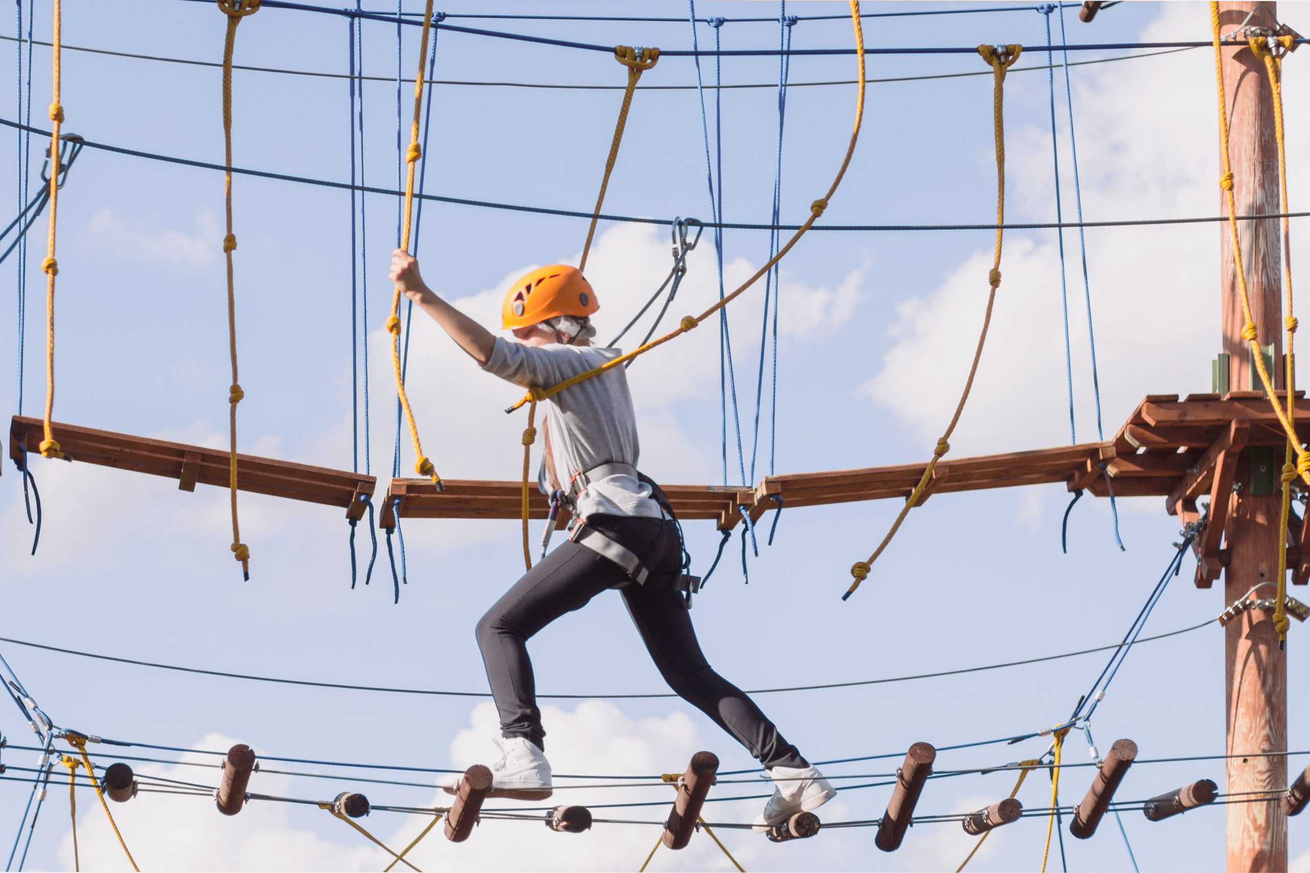 A school girl climbs in an adventure rope park on a summer day