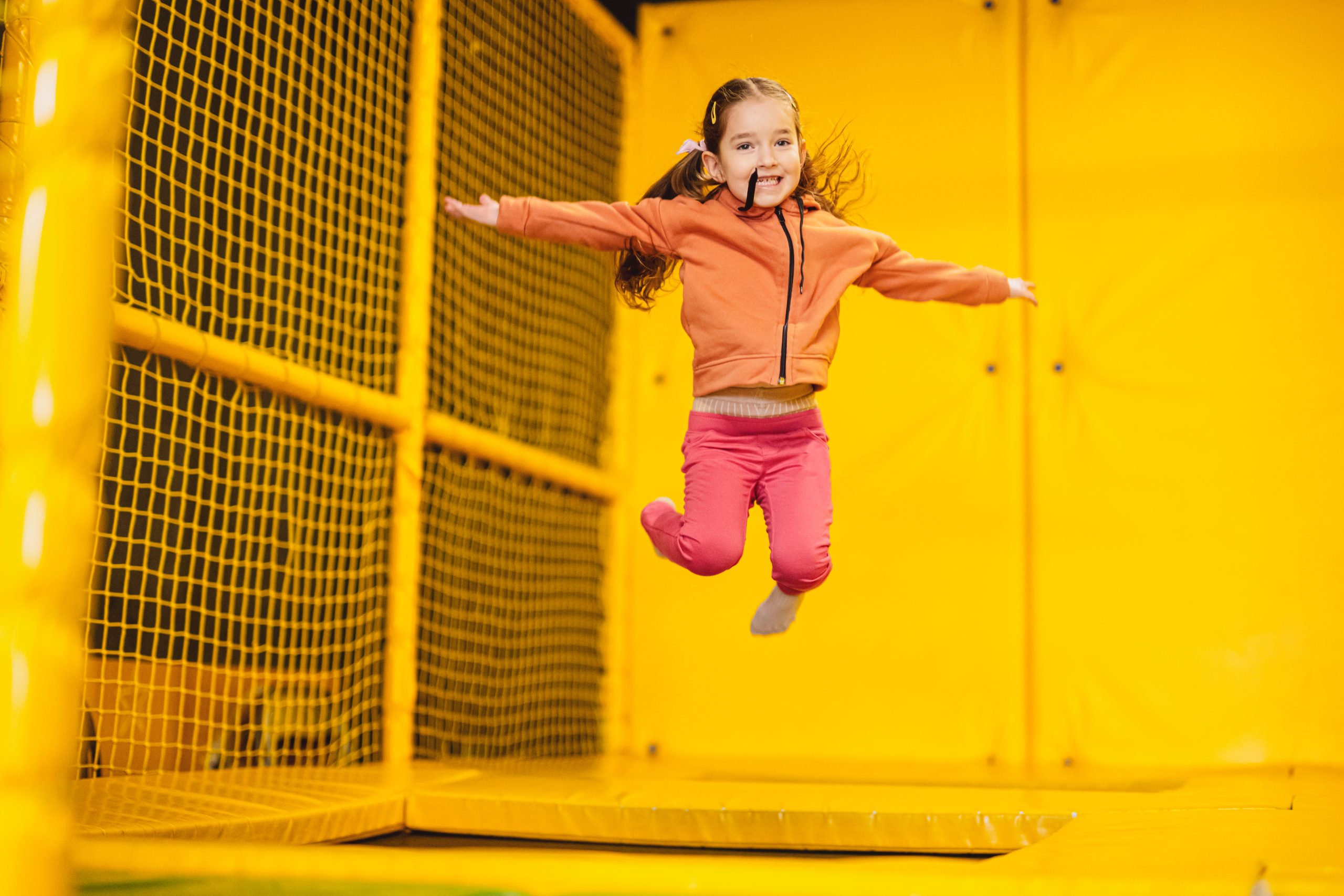 Little girl kid jumping on trampoline at yellow playground park. Child in motion during active entertaiments.